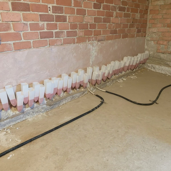 Injektionsverfahren bei feuchter Kellerwand: Flüssiges Paraffin wird in Bohrlöcher injiziert, um eine Horizontalsperre zu erstellen und aufsteigende Feuchtigkeit im Keller zu stoppen